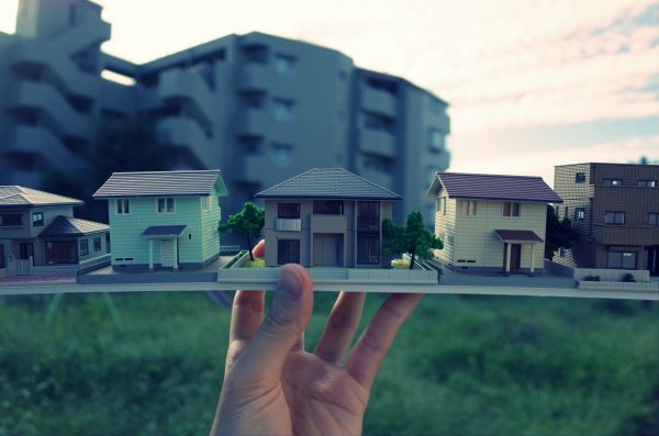 住宅地を背景に手に持った住宅模型の写真